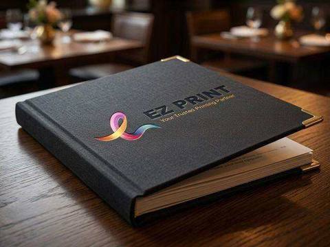 A luxury hardcover hospitality menu book with brass corner protectors and debossed EZ Print ribbon mark on an oak table.